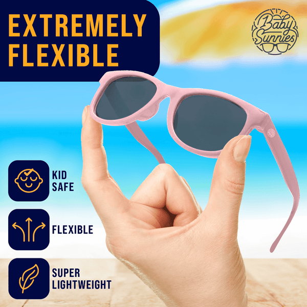 Kids pink polarized sunglasses, flexible and lightweight, held in hand with beach background.